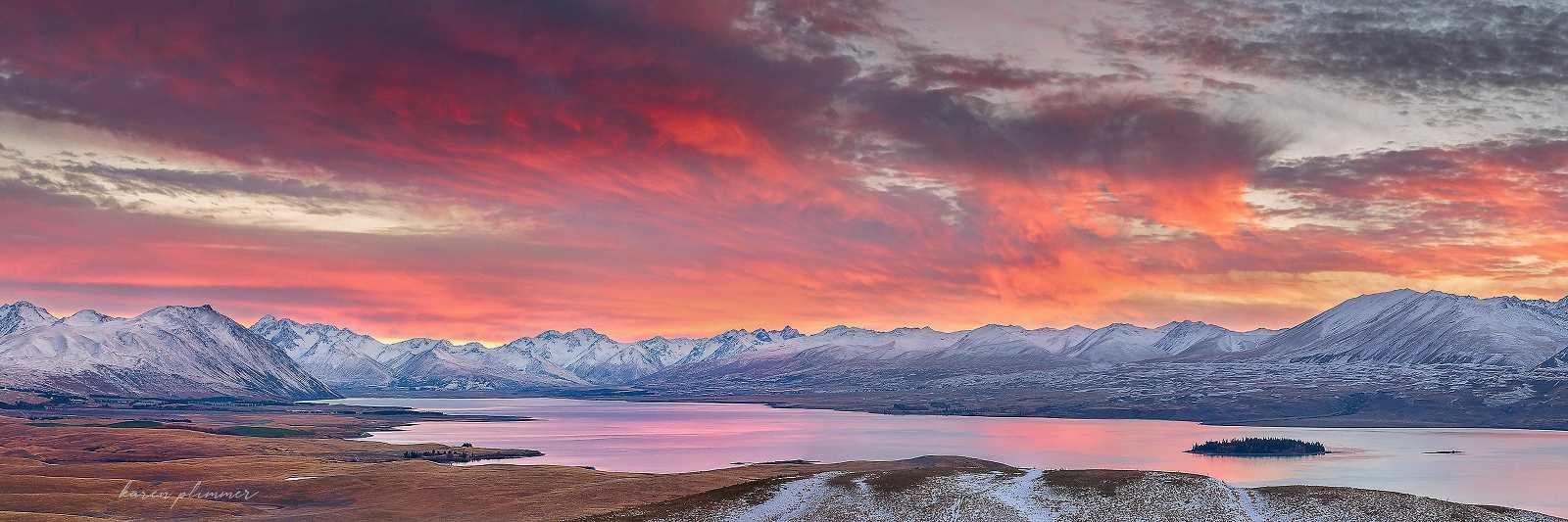 A view of the snow-covered mountains surrounding Lake Tekapo, New Zealand with an very colourful sunrise.